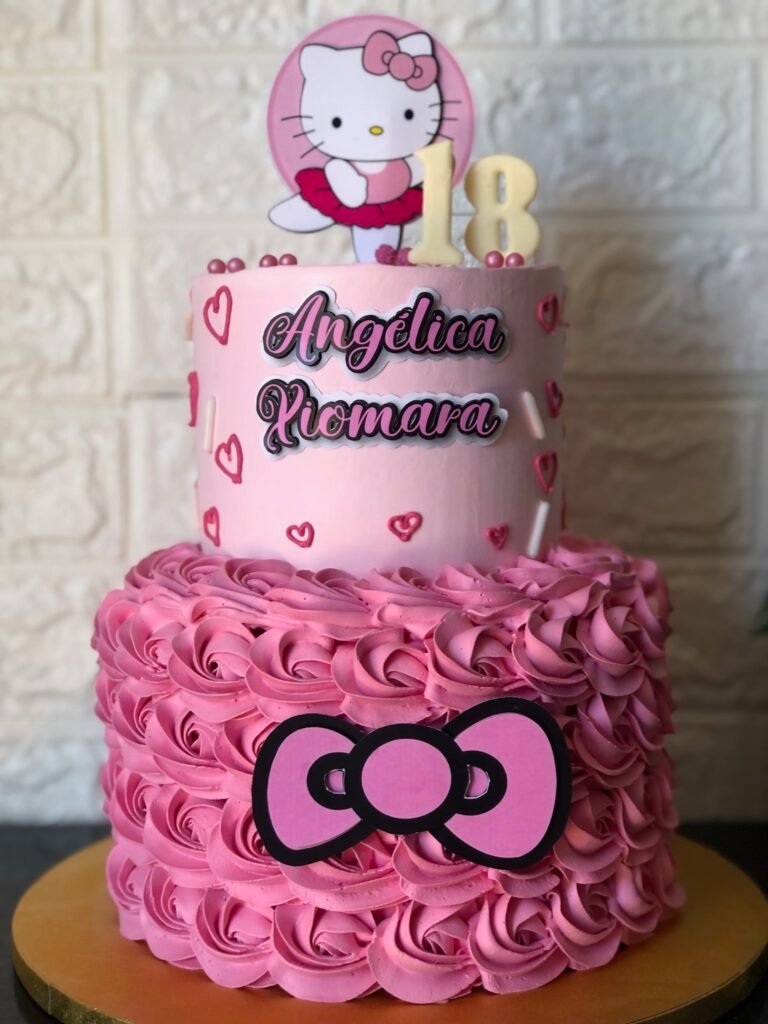 Tarta infantil de dos pisos decorada con temática de Hello Kitty en tonos rosas y nombre personalizado.